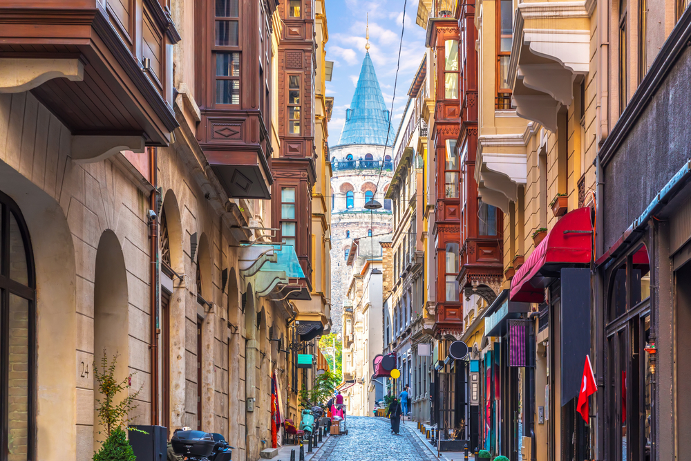 Narrow street with colorful buildings, leading to a historic tower under a blue sky.
