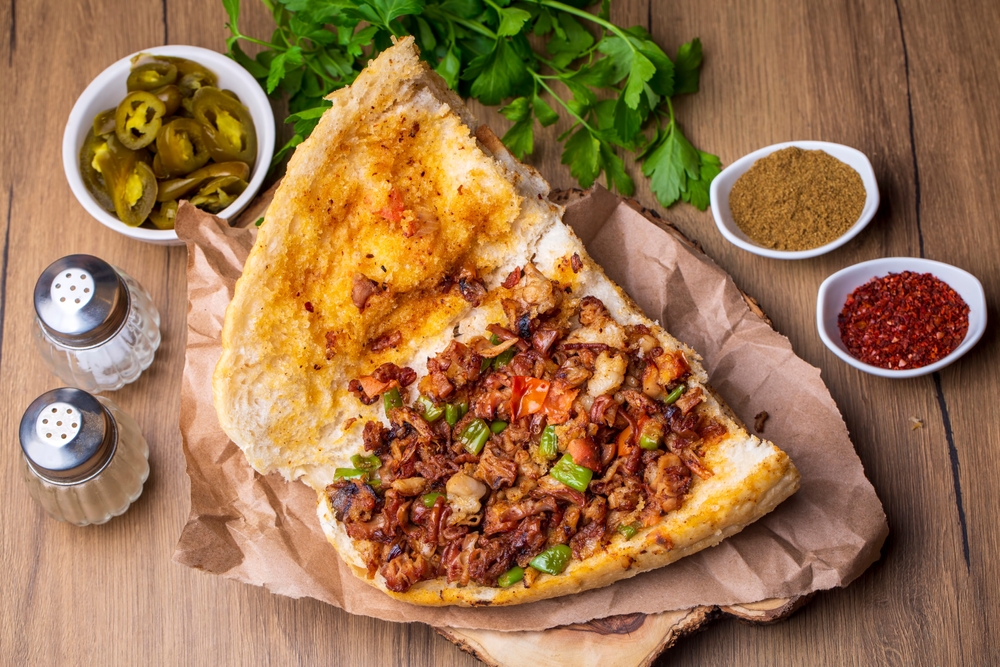 Piece of flatbread with spiced meat and vegetables, surrounded by spices and jalapeños.