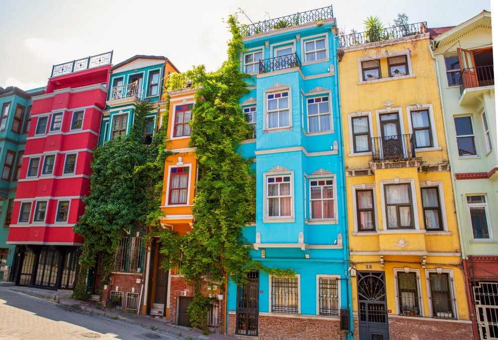 Istanbul Balat Fener Colorful buildings lined up, with red, orange, turquoise, and yellow facades, and lush greenery growing on one.