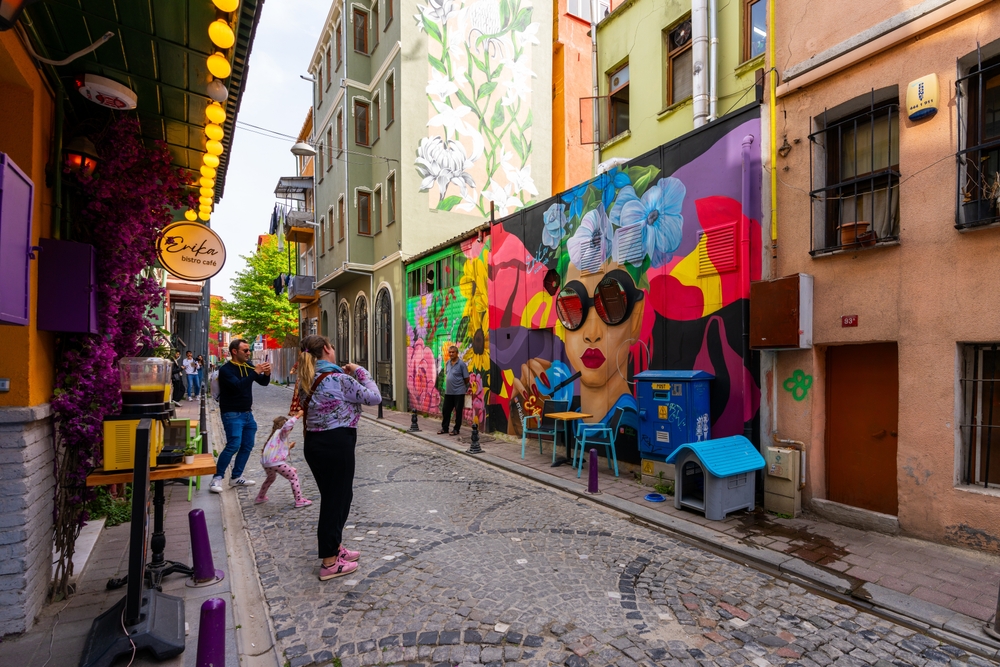 Colorful street with mural, people walking, and lively buildings.
